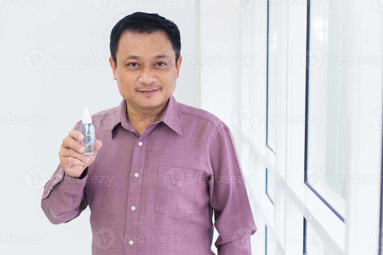 Asian man in pink shirt holds a alcohol spray bottle. photo