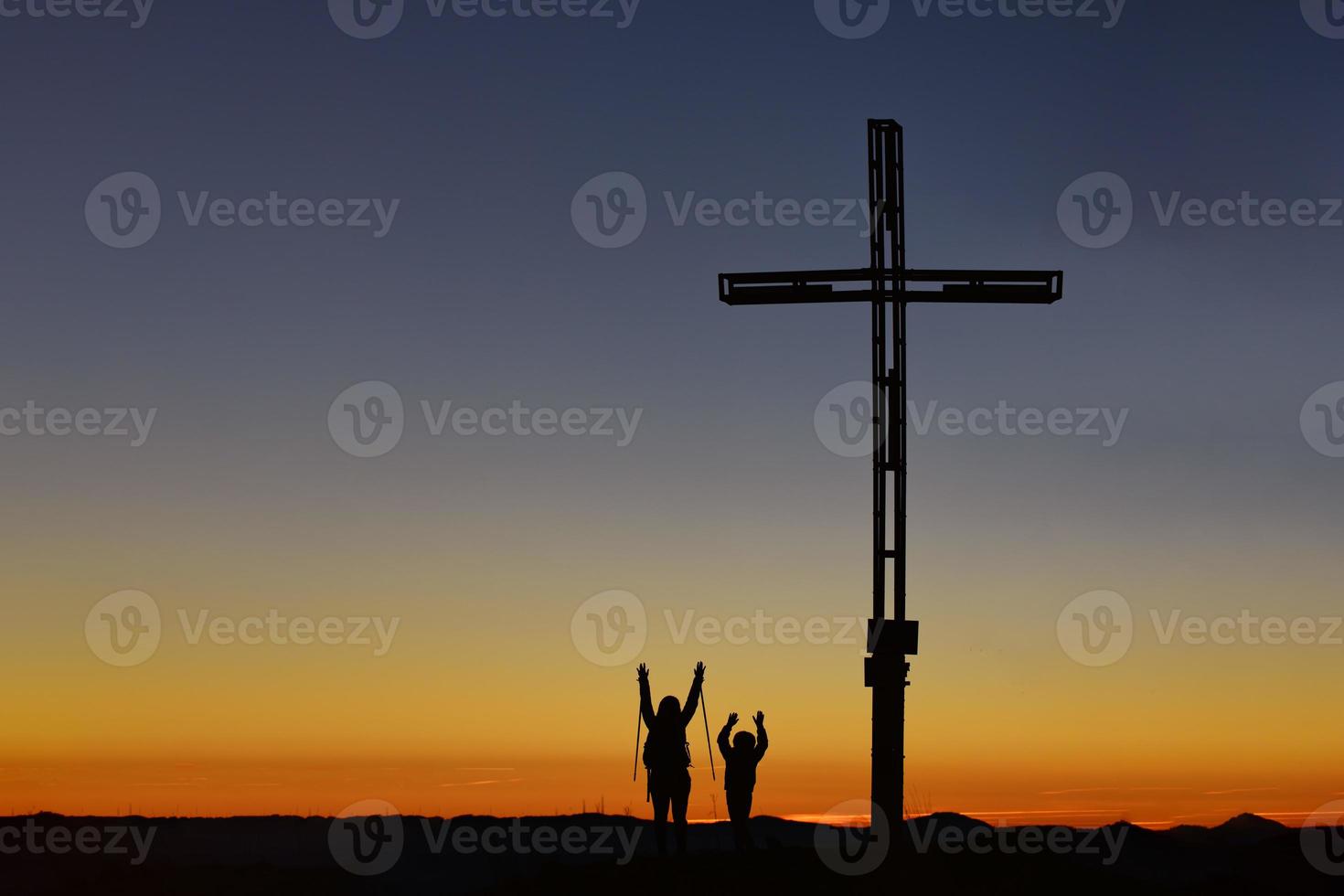 Mom with child on top of the mountain near the cross raise their arms in victory photo