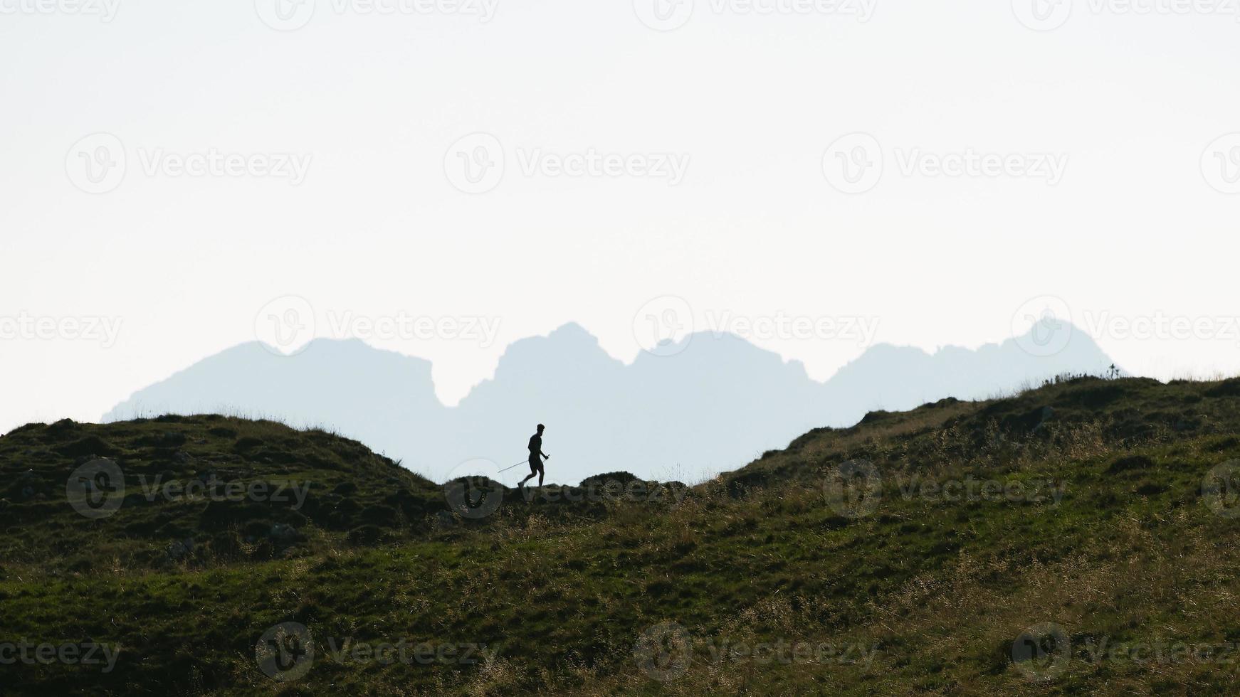 Silhouette of a man who practices Nordic walking in the mountains photo