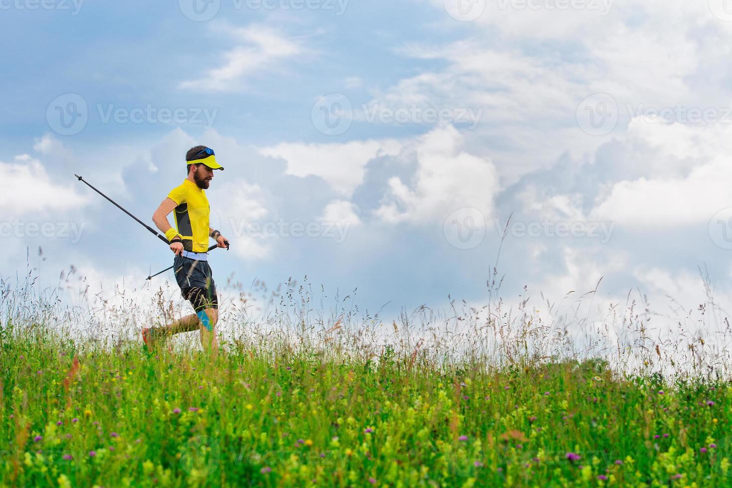 Young man runs down in the green grass while practicing Nordic walking photo