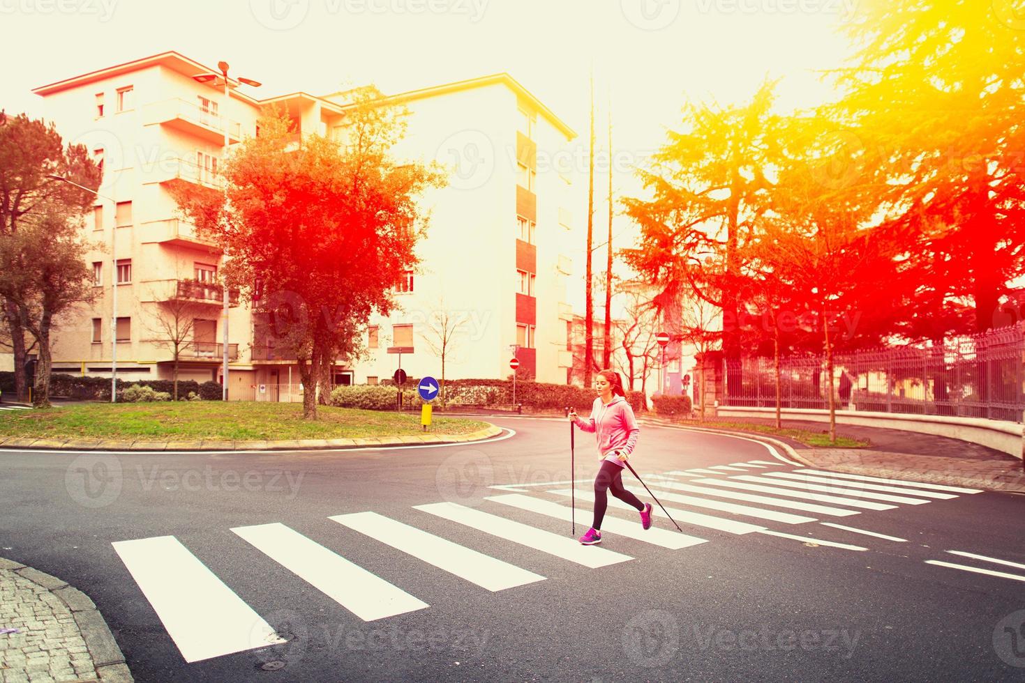 chica practicando marcha nórdica en la ciudad, pasando el paso de peatones foto