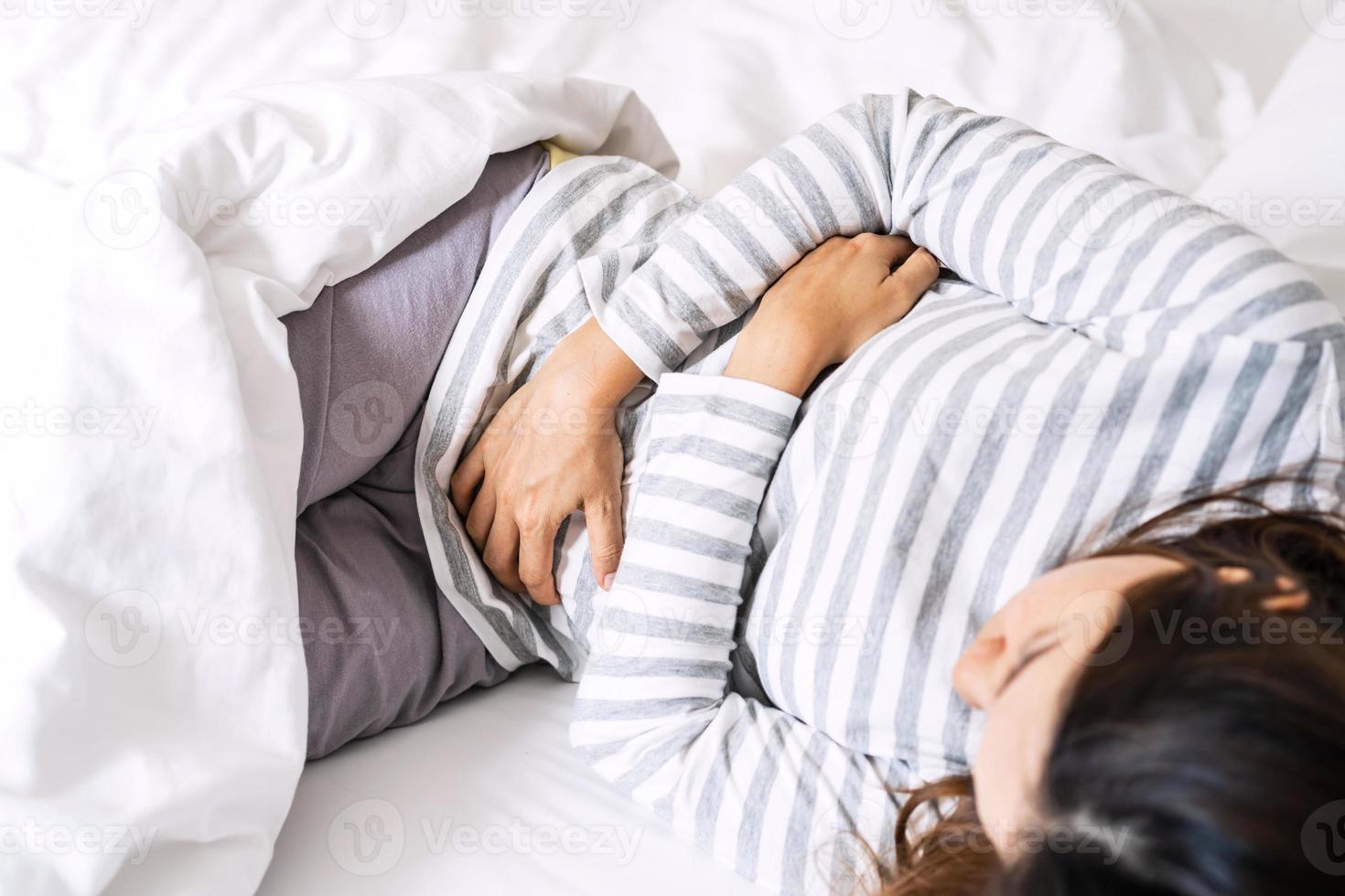 mujer joven con dolor de estómago en la cama. concepto de problemas de calambres menstruales foto