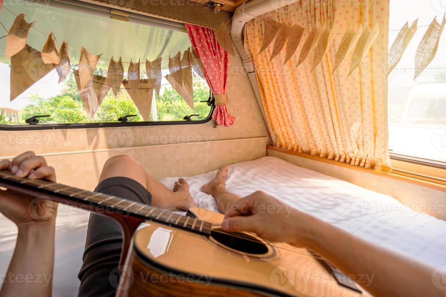 Young man traveler laying in camper van and playing guitar while road trip traveling on vacation photo