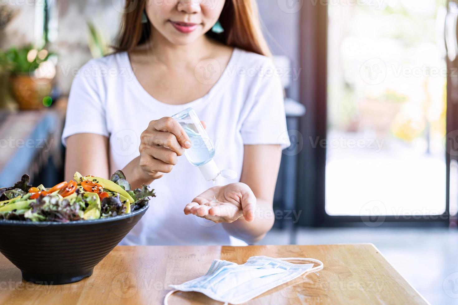 Young woman using alcohol gel sanitizer to avoid infections corona virus and bacteria before meals in restaurant, New normal lifestyle concept photo