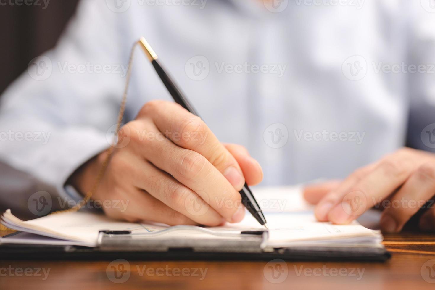 business man person using a pen to sign a agreement document paper to approve by signature, hand of businessman working on finance lawyer contract paperwork in office, concept of deal on business desk photo
