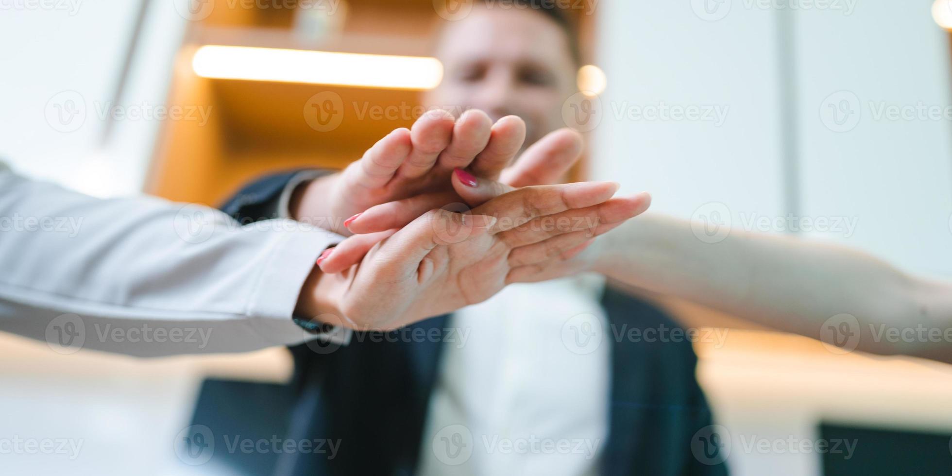 Team of young male and female employees stacking hands on top of each others to depict unity and harmony amongst colleagues for project and positive work environment photo