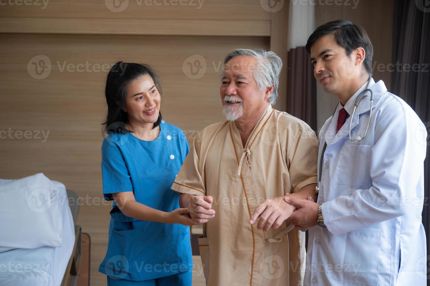 paciente varón mayor sentado en silla de ruedas en el hospital sonriendo y hablando y mostrando algo fuera de la ventana a un apuesto doctor en bata de laboratorio foto