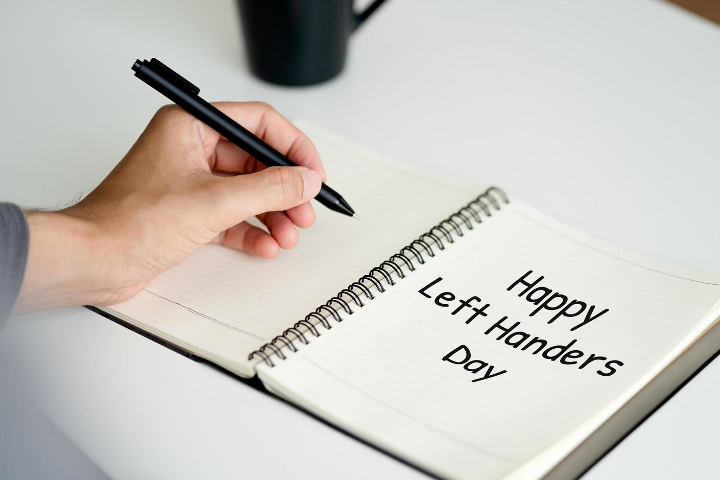 left handed man writes in a notebook on the table, International Left-handers Day photo