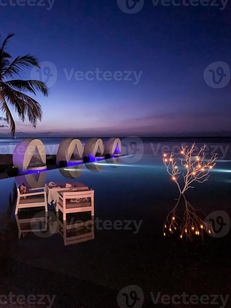 piscina al atardecer con mesa de cena romántica privada y decoración ligera. cielo al atardecer, luna de miel, concepto de viaje de aniversario. vacaciones en pareja en destinos de lujo foto