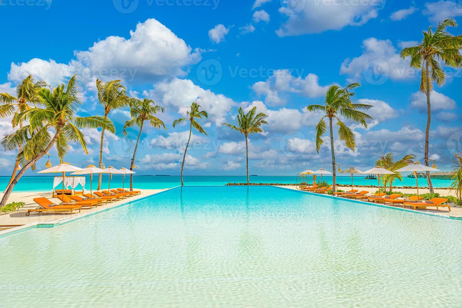 Outdoor tourism landscape. Luxurious beach resort with swimming pool and beach chairs or loungers under umbrellas with palm trees and blue sky. Summer travel and vacation background concept photo