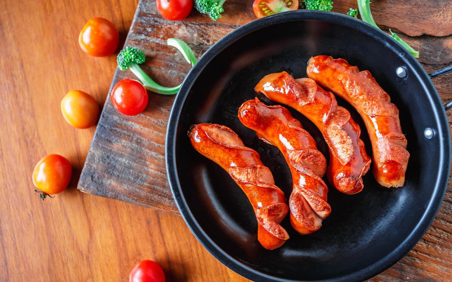 salchichas fritas en una sartén con tomates y brócoli foto