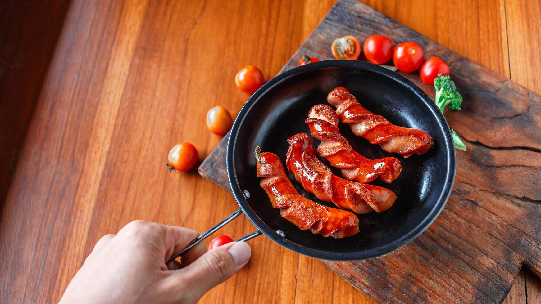 Fried sausage in a black pan in chef hands. photo