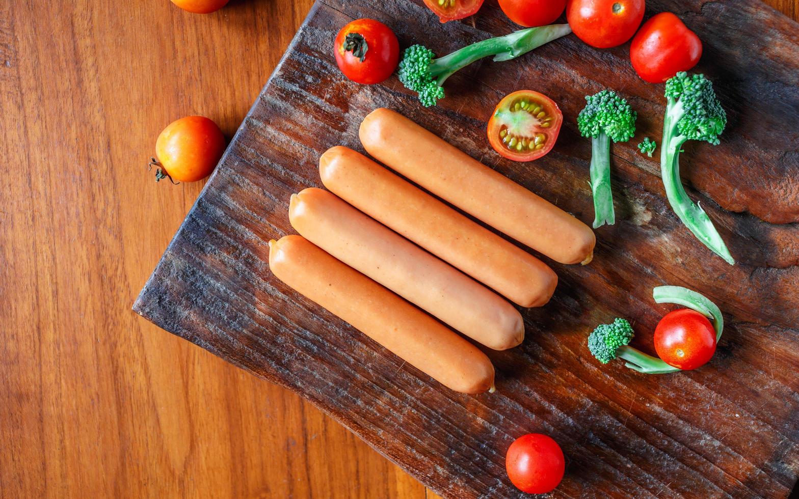 salchicha cruda en una tabla de cortar de madera con brócoli y tomates foto