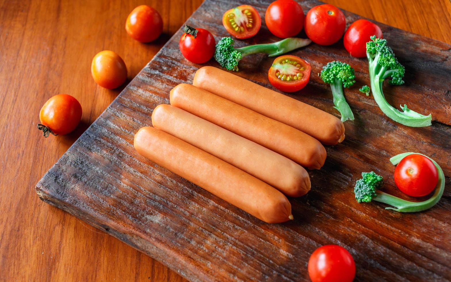 salchicha cruda en una tabla de cortar de madera con brócoli y tomates foto