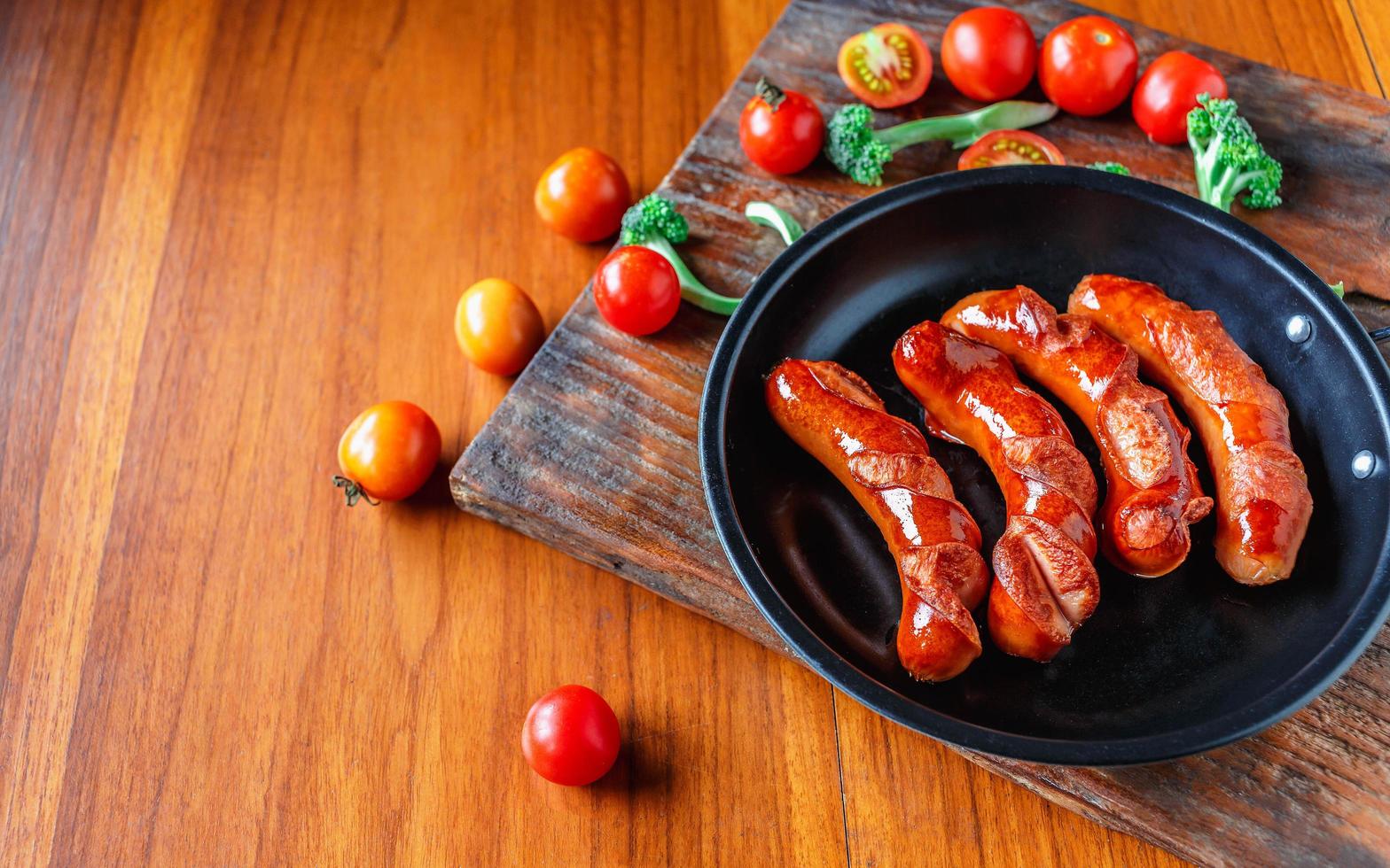 salchichas fritas en una sartén con tomates y brócoli foto