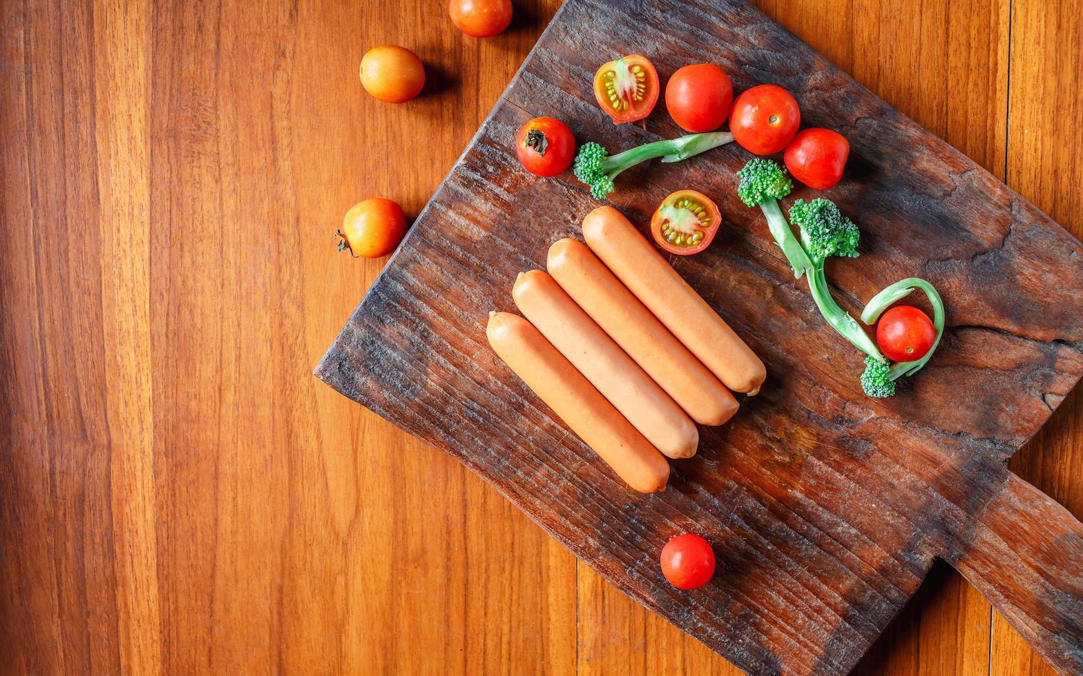 salchicha cruda en una tabla de cortar de madera con brócoli y tomates foto