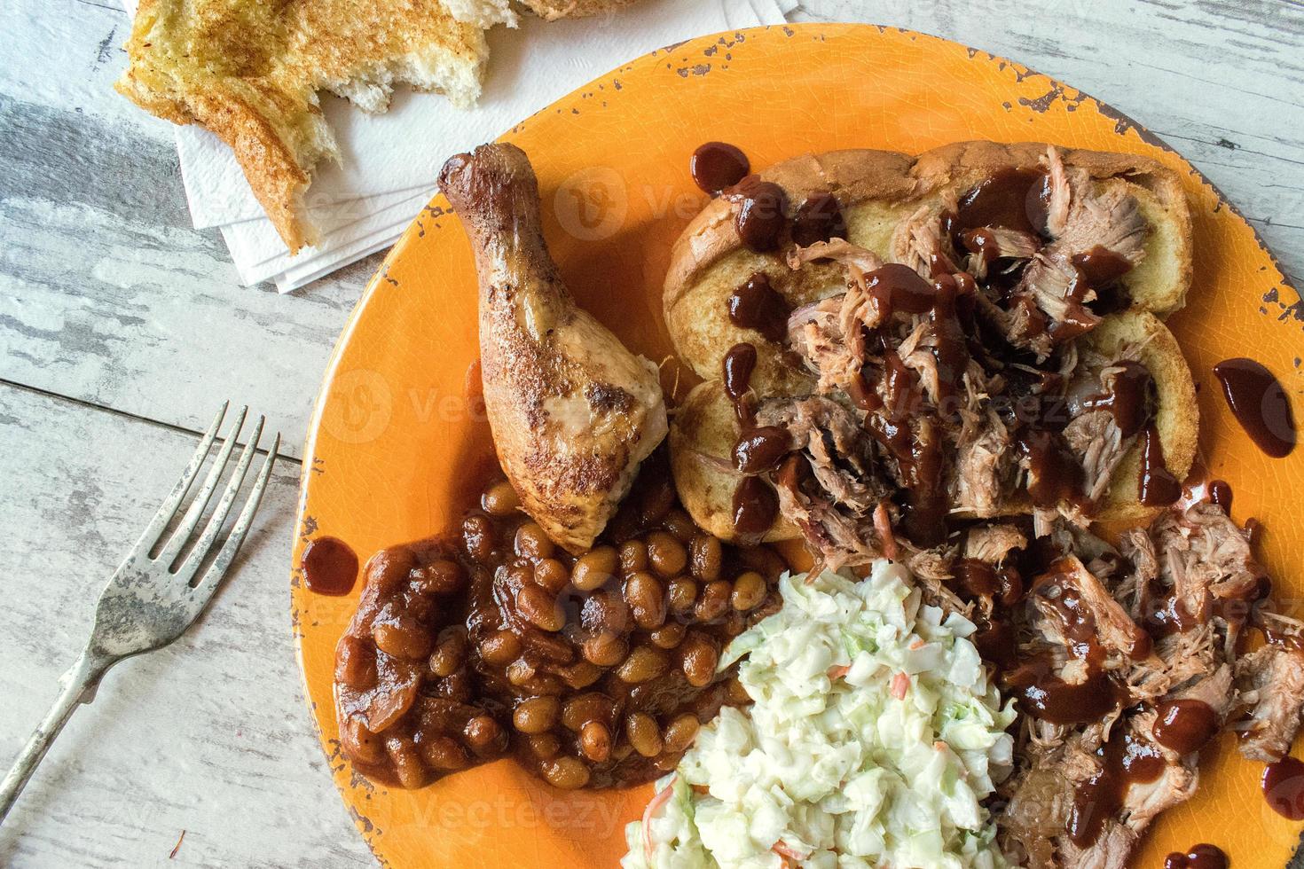 plate of barbecue brisket with chicken leg, baked beans, and coleslaw flat lay photo