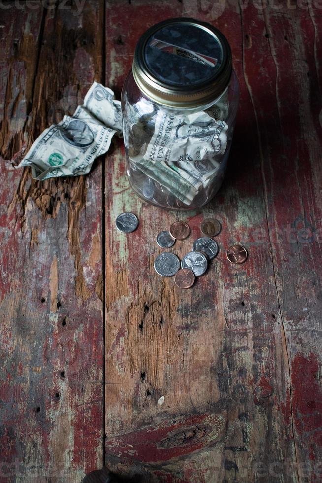 tarro de dinero con monedas y billetes en mesa de madera rústica foto