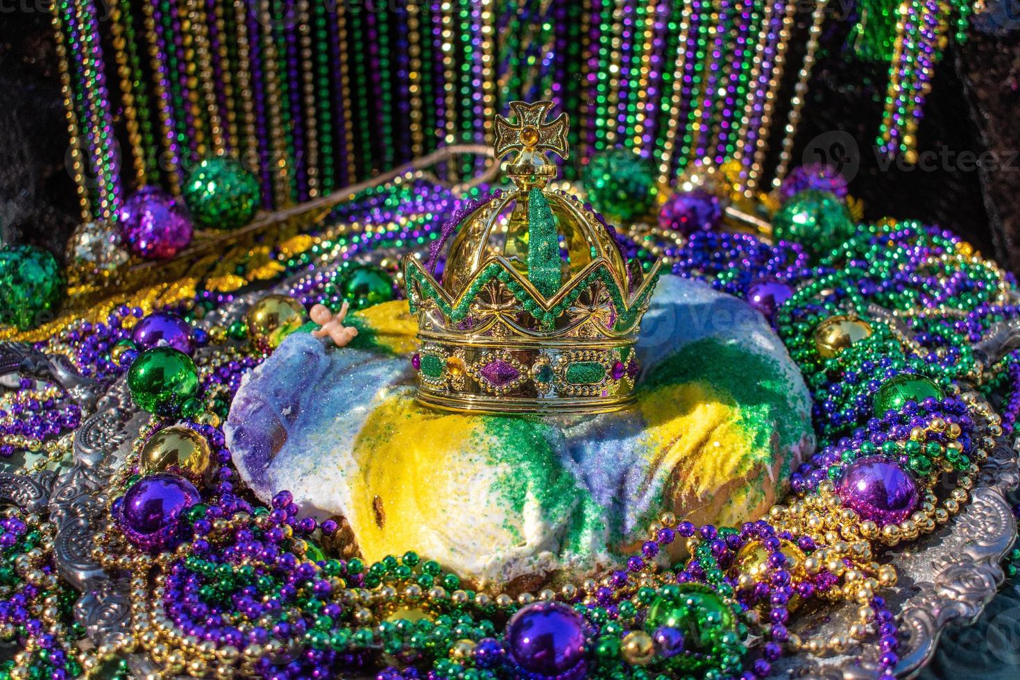 Mardi Gras King Cake topped with crown surrounded by beads and decorations photo