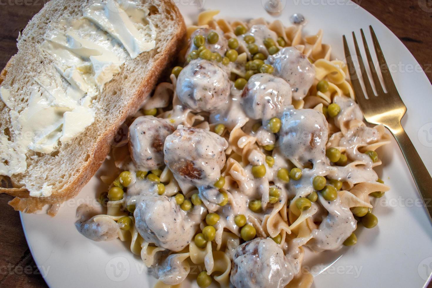 Plated homemade Swedish Meatballs on pasta with peas and buttered bread photo