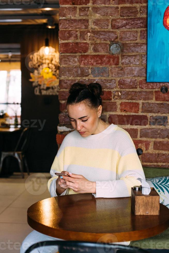 A young girl at a table in a cafe looks at the phone, smiles and texting. photo