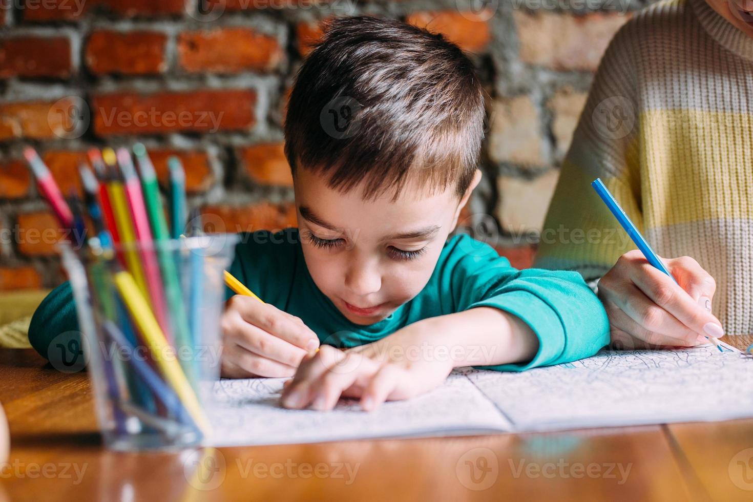 Portrait of a cute happy preschool boy at home or in a cafe draws. photo