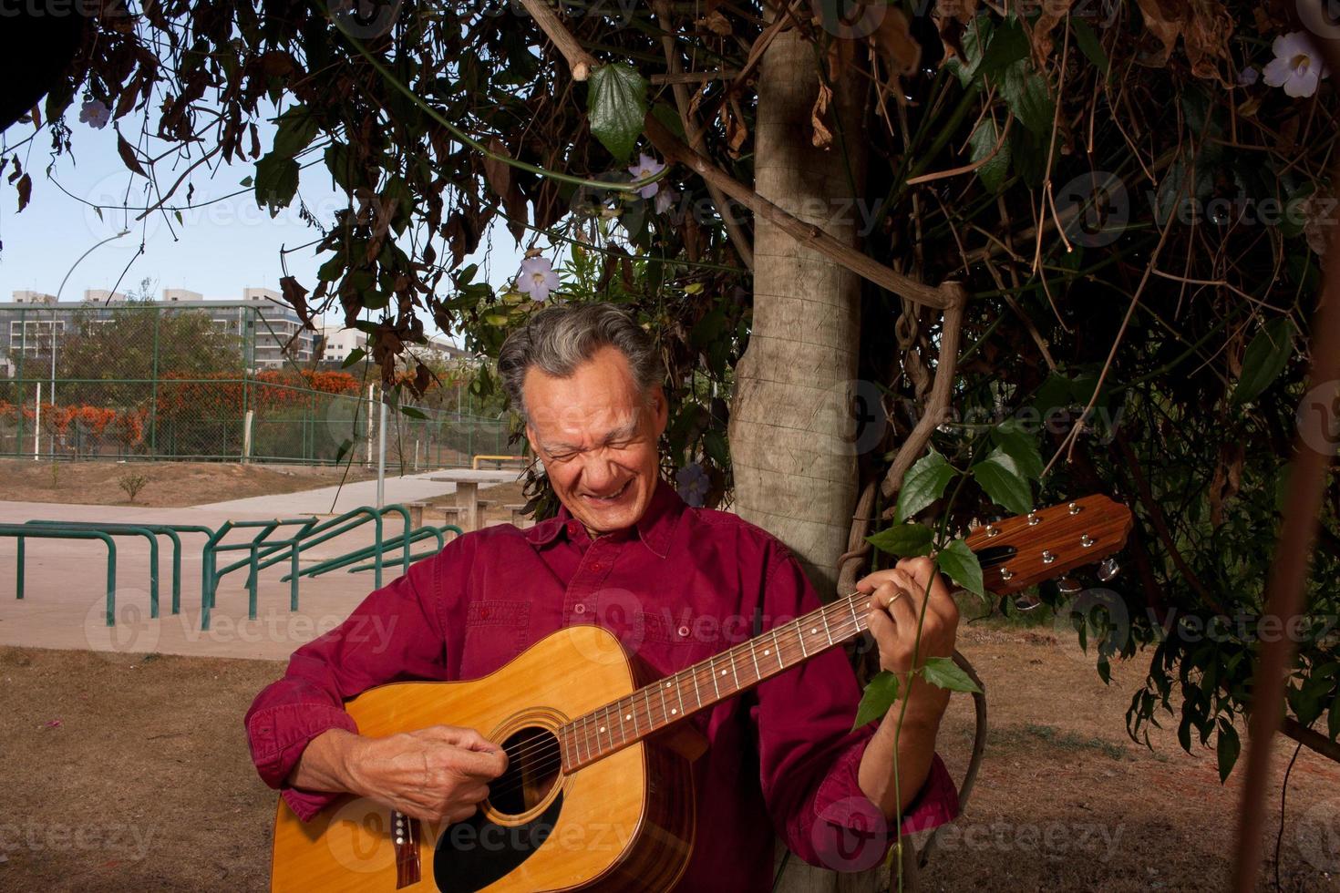 Happy Mature Man singing and playing his acoustic guitar in the park photo