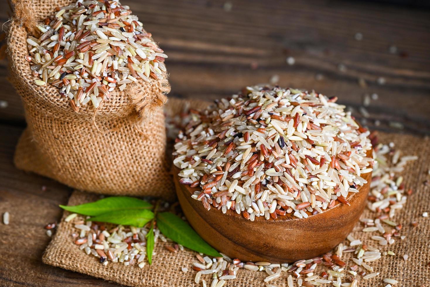 arroz integral en un tazón de madera y el fondo del saco, varios colores de arroz crudo, arroz tailandés mezclado para cocinar alimentos, arroz loonzain, marrón, negro, rojo, blanco, púrpura, alimentos saludables. foto