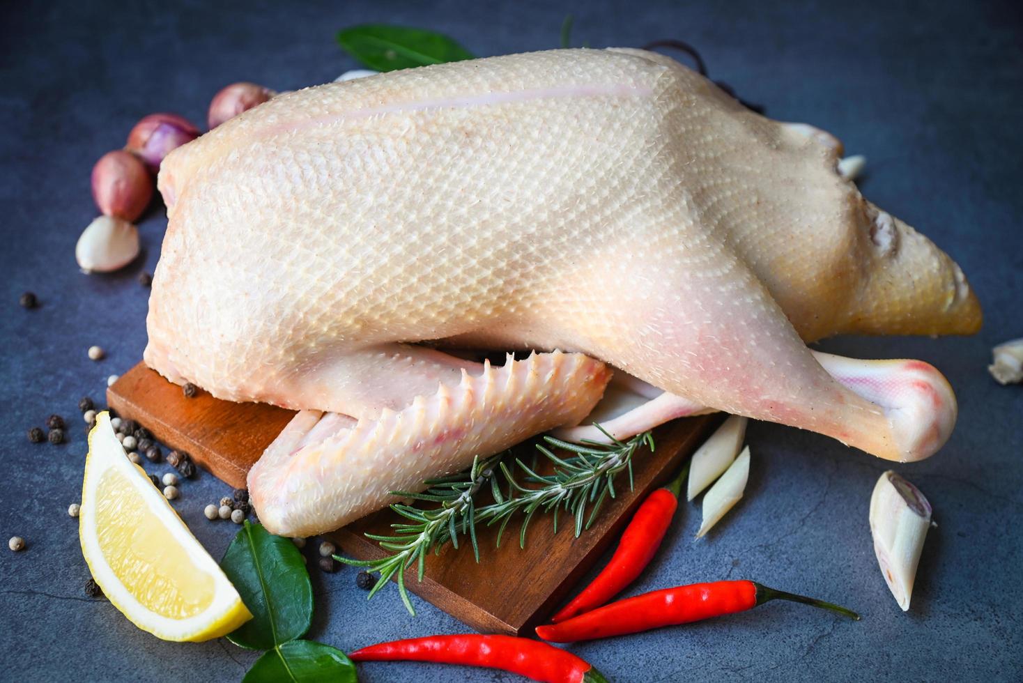 pato crudo con especias listo para cocinar sobre fondo negro, carne de pato fresca en el plato para la comida, pato entero y ajo picante de limón y romero foto