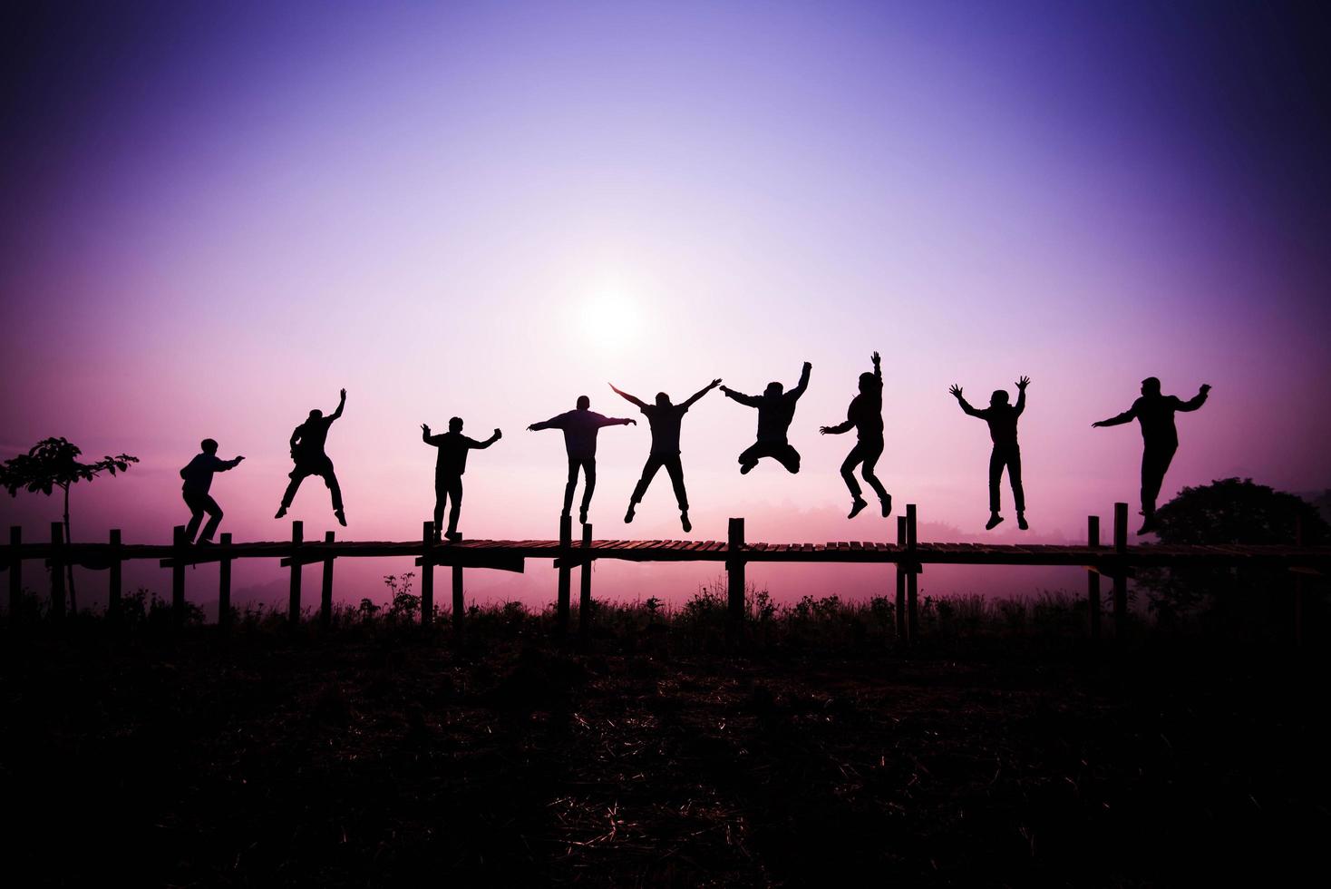 Silhouette Jumping team friends jumping on the wooden bridge on hill - happy and funny enjoy jumping people with sunrise photo