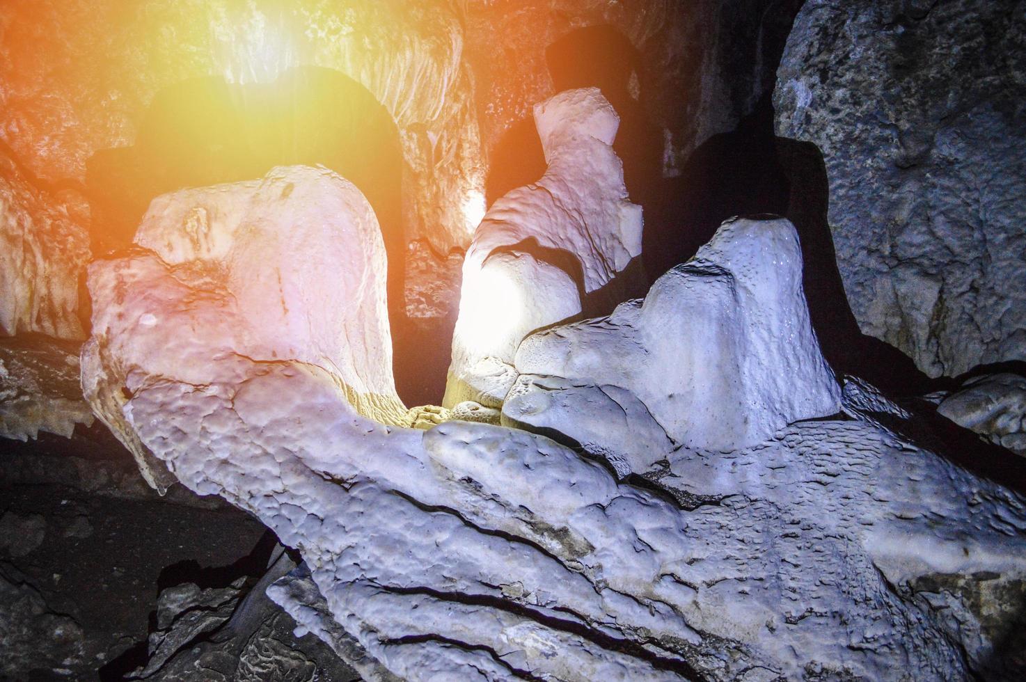 Stalagmite and stalactite stone in dark cave with light from flashlight photo