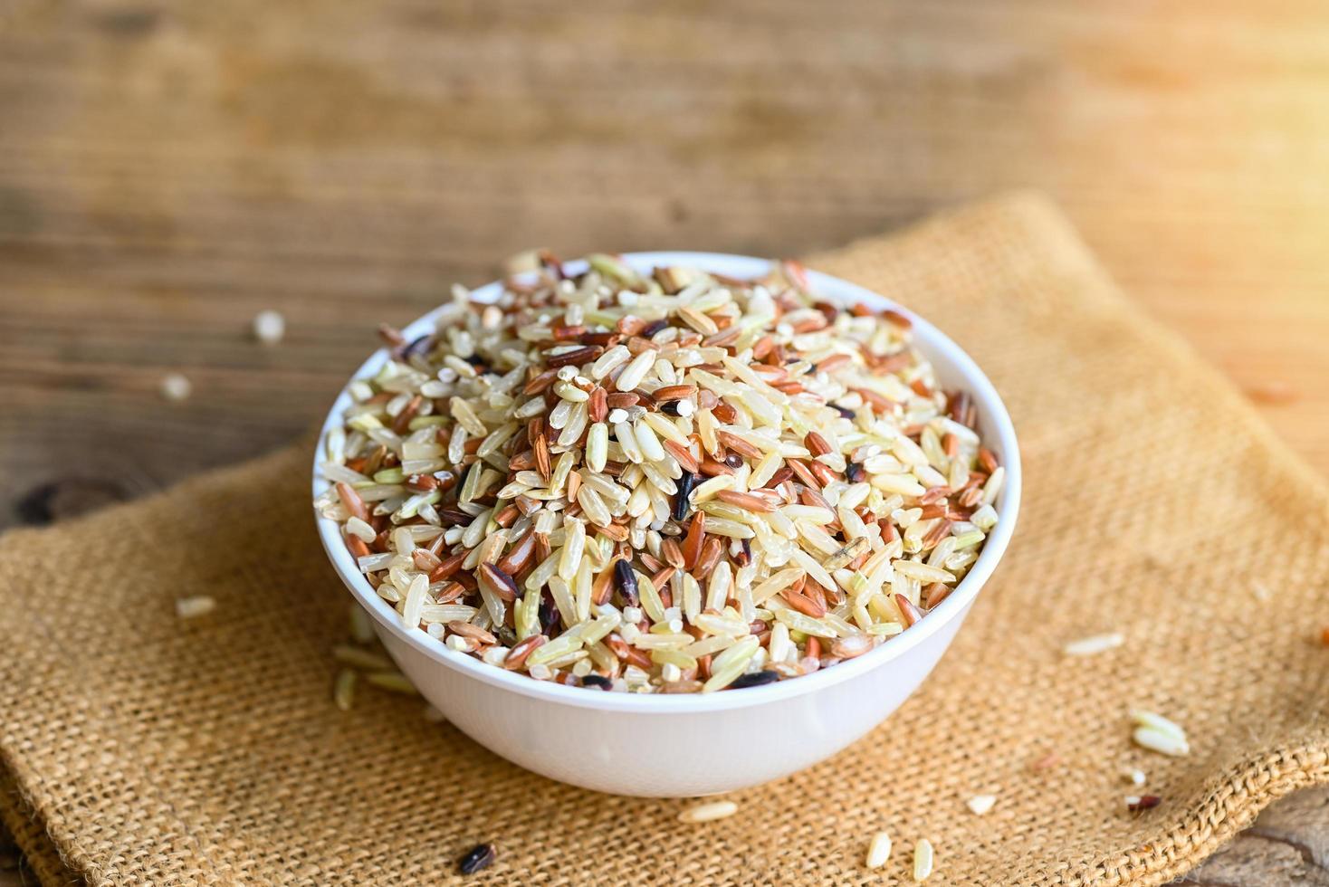 brown rice on white bowl wooden background , raw various rice color mixed thai rice for cooking food , Loonzain rice brown black red white purple health food. photo