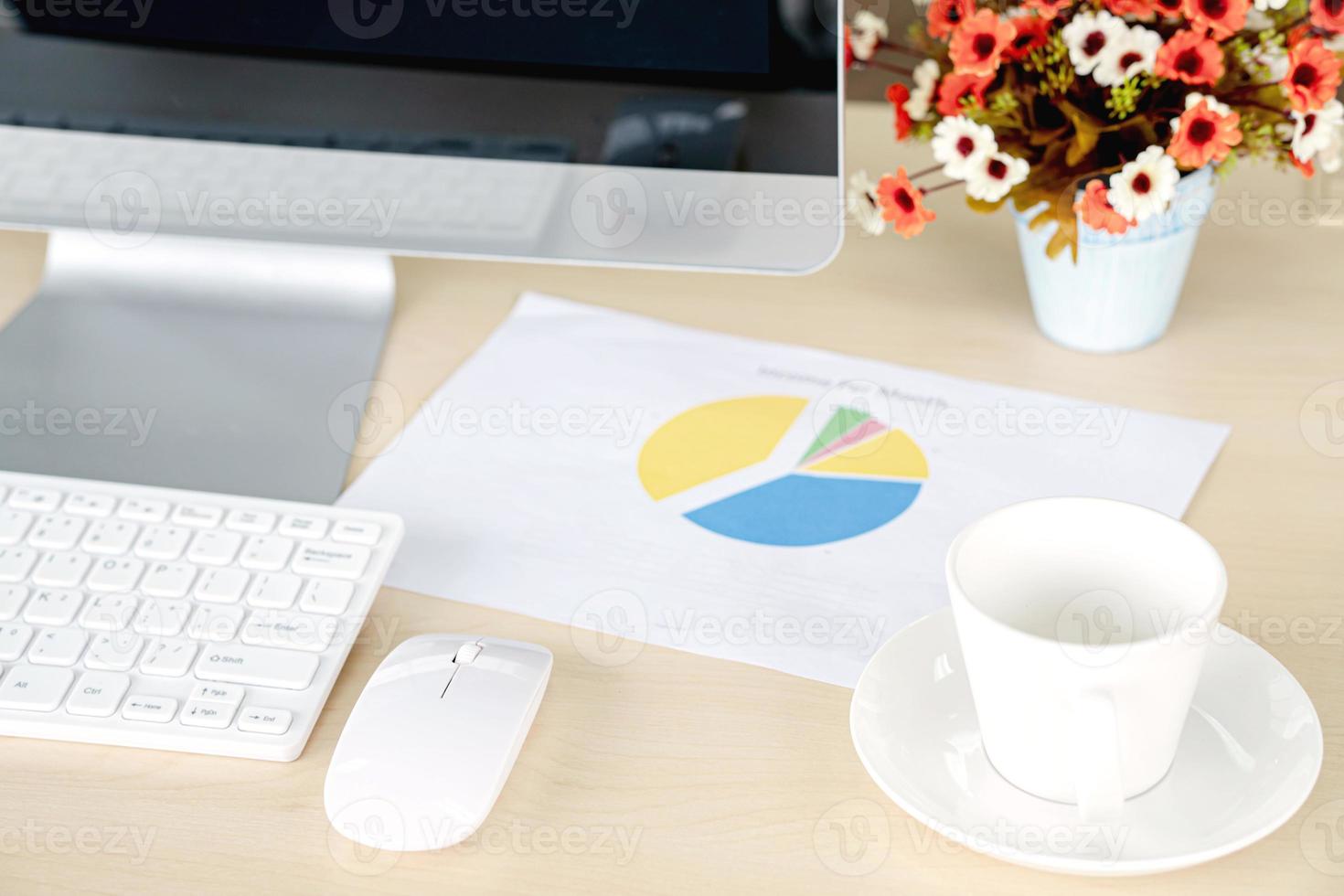 Business and workplace concept. Cup of hot coffee on work desk with computer keyboard and papers graphs photo