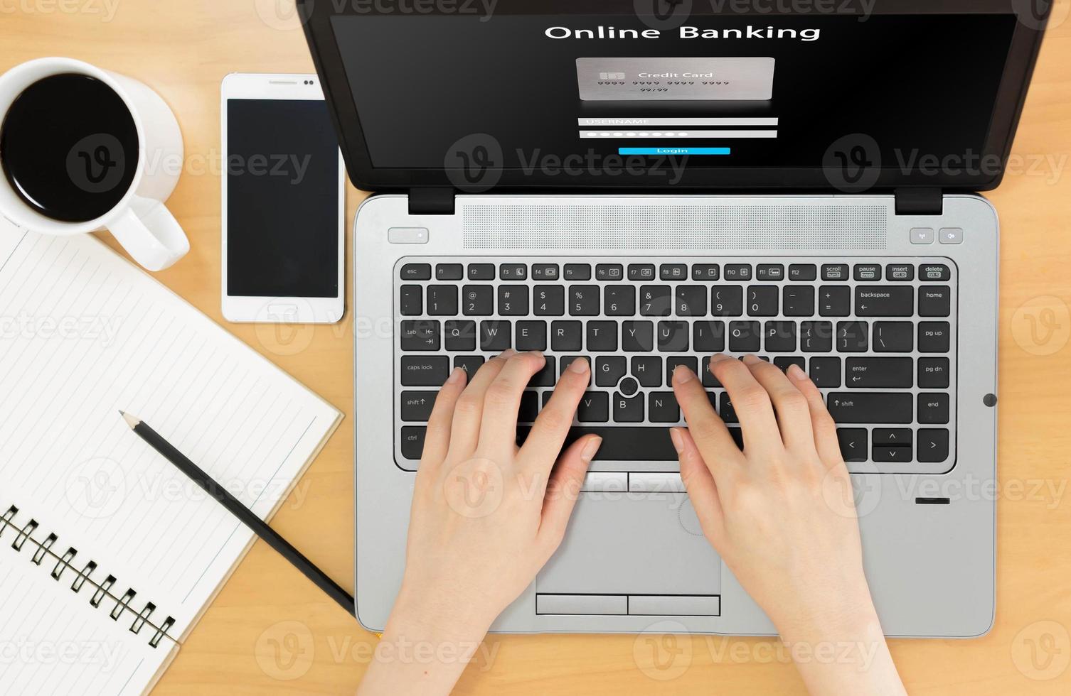 vista superior del espacio de trabajo empresarial a la banca en línea, cuaderno, taza de café y manos femeninas escribiendo en el teclado foto