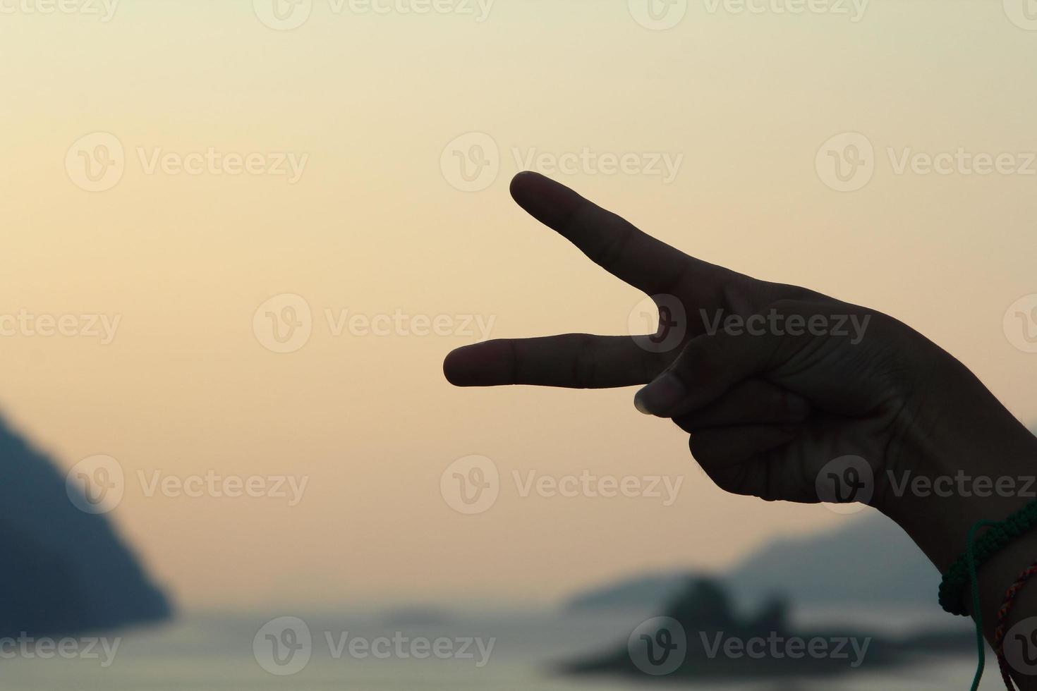 Two-finger symbol, index finger and middle finger, symbol of peace on the background Mountains, rivers and blue skies Attractive nature photo