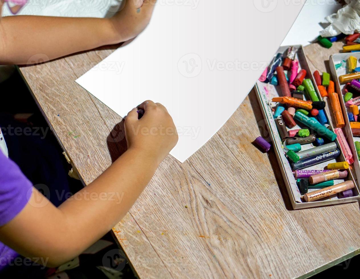 Closeup and crop hands of student holding crayon draw and painting on white paper in art classroom. photo
