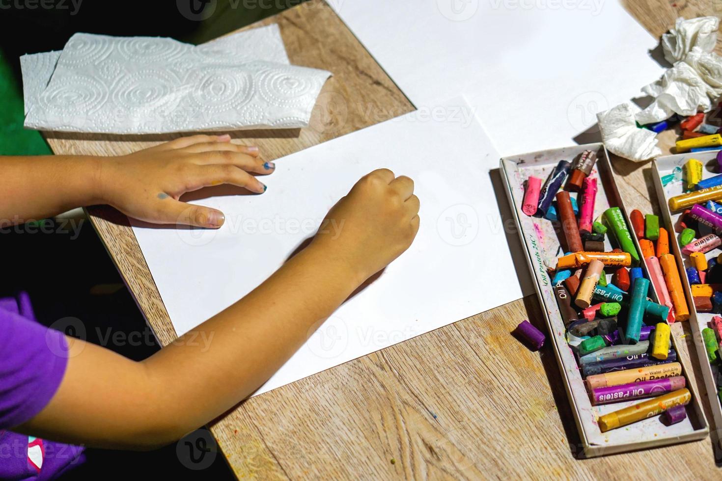 cierre y recorte las manos de un estudiante que sostiene un dibujo de crayón y pinta sobre papel blanco en el aula de arte. foto