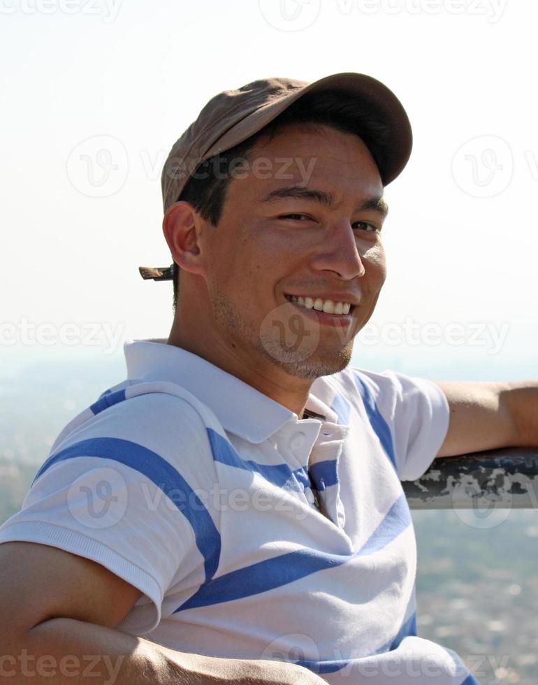 apuesto y sonriente joven sentado al sol con la ciudad de atenas, grecia, en el fondo foto