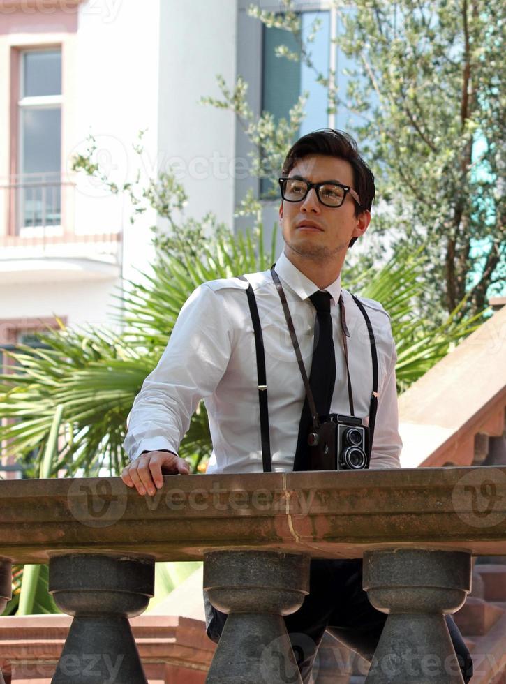 Young man wearing suspenders and glasses looking out from a large terrace photo