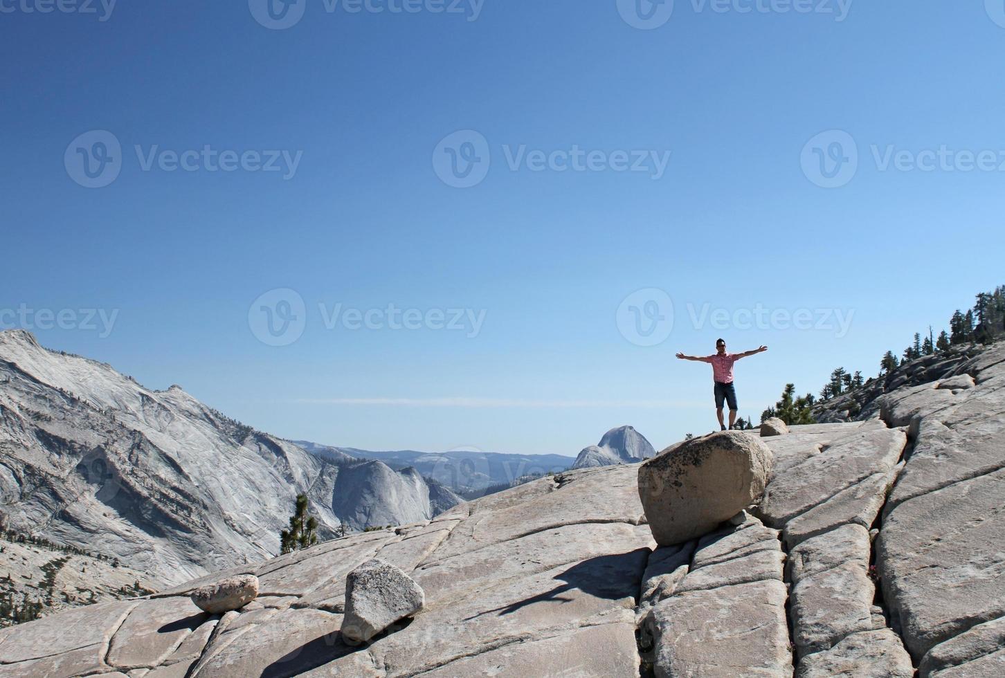 Young man standing on a rock with raised arms in front of a Yosemite mountain range panorama photo