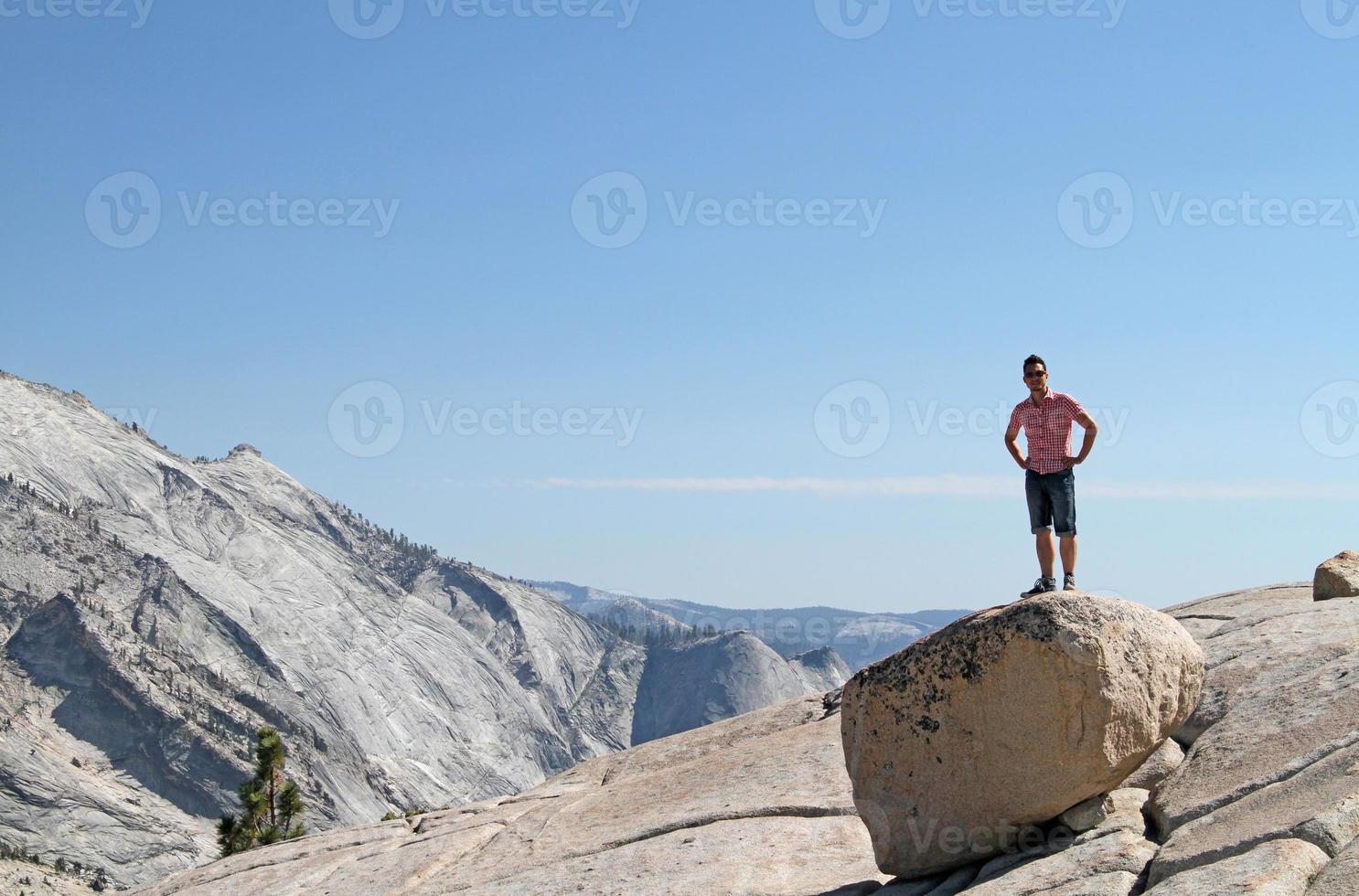 Young man standing on a rock in front of a Yosemite mountain range panorama photo
