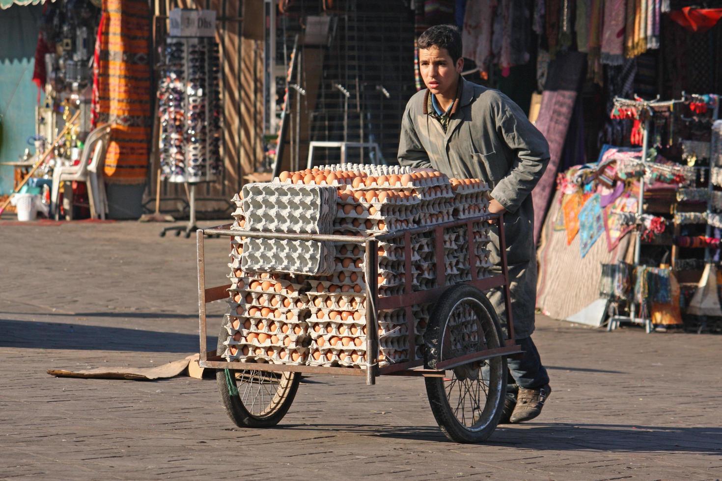 Marrakech, Morocco - September 12, 2021 - A tired boy pushes a cart filled with egg cartons through the old town of Marrakech photo