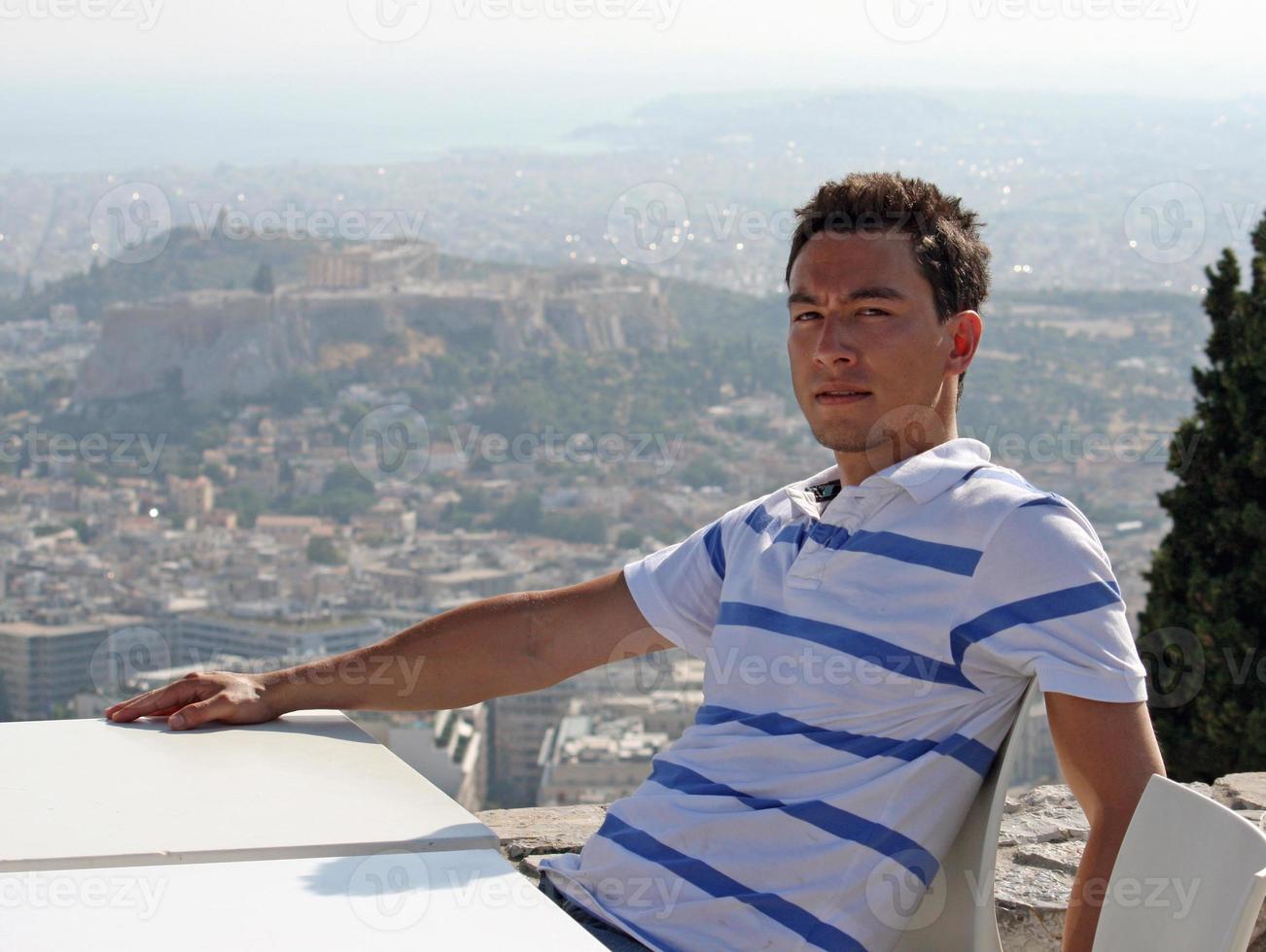 Handsome young man with a serious face sitting in the sun with the city of Athens, Greece, in the background photo
