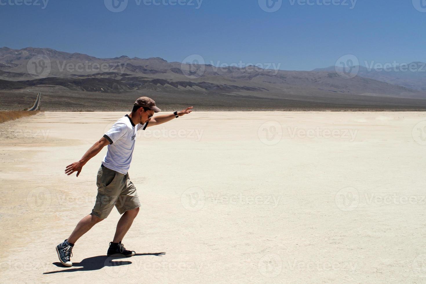 joven con gafas de sol y pantalones cortos agitando los brazos como si estuviera sobre una tabla de surf en medio del valle de la muerte foto