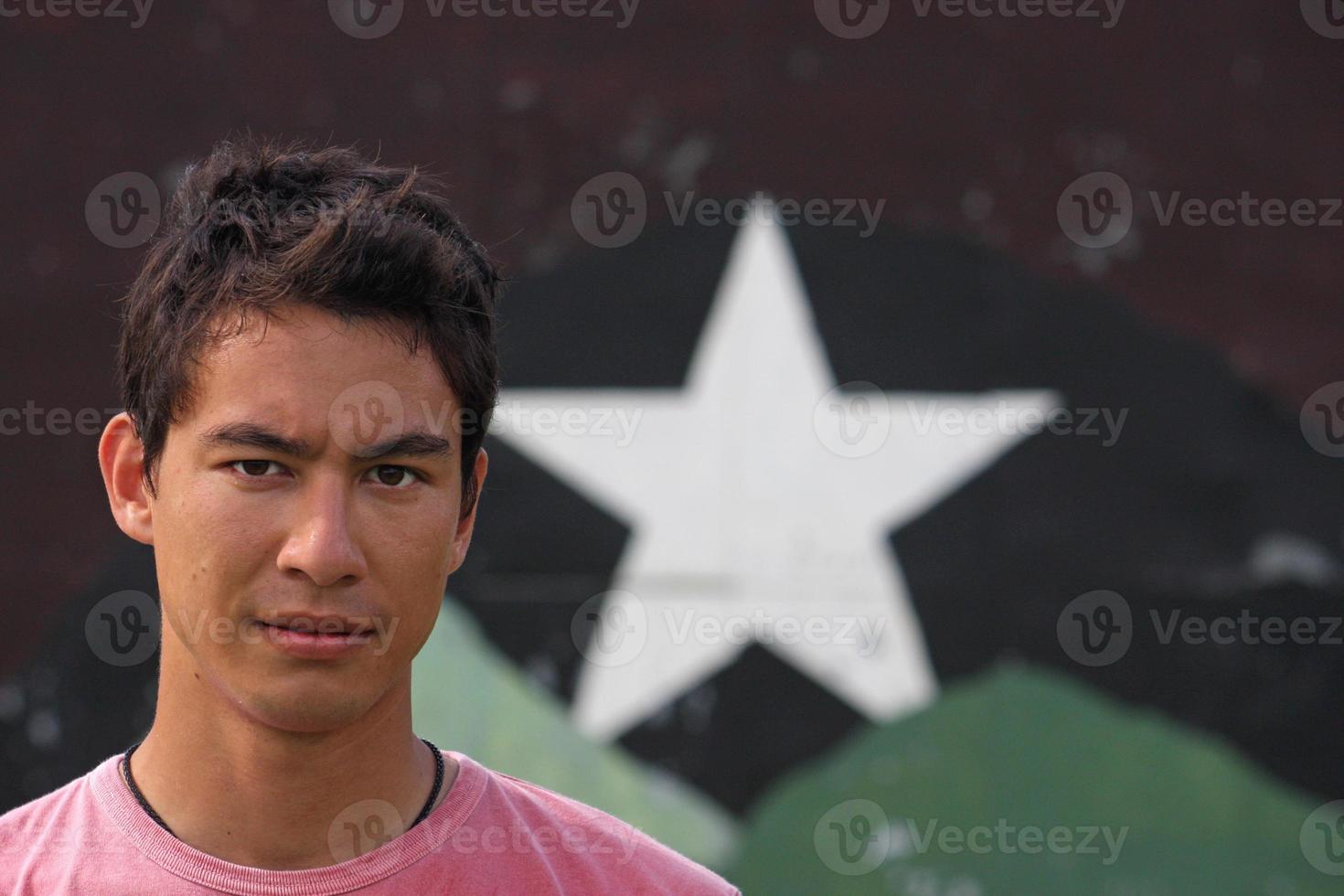 joven adulto eurasiático mirando a la cámara con una mirada segura y seria, mientras está de pie frente a una pared con una estrella. foto