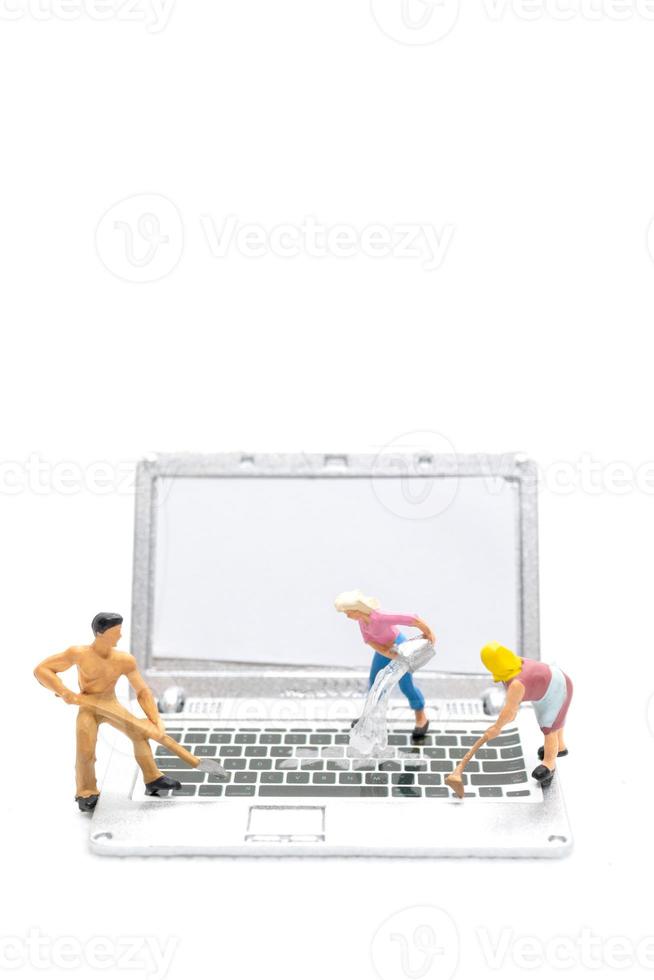 Miniature people cleaning laptop computer on white background photo