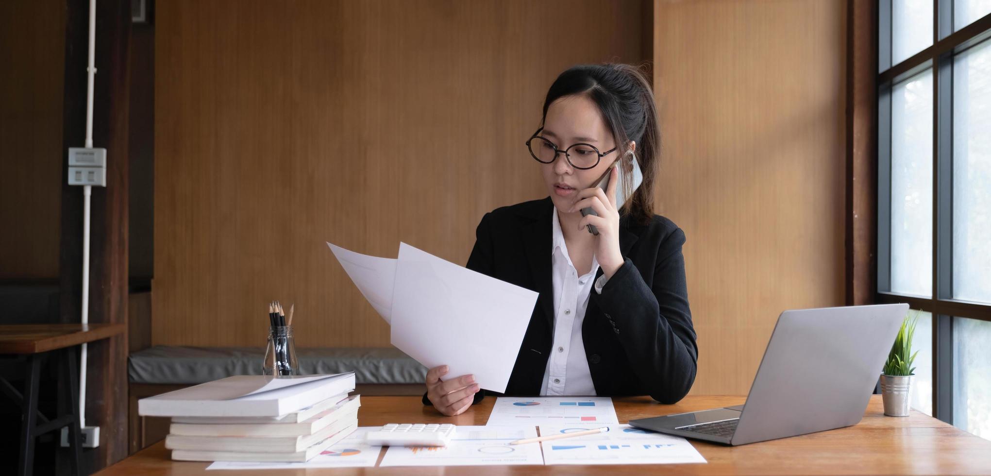 una mujer de negocios asiática seria que usa una laptop mirando la computadora hablando por teléfono consulta al cliente sentada en el escritorio, la gerente de ventas enfocada hace una llamada de negocios móvil para discutir el trabajo con el cliente en la oficina foto