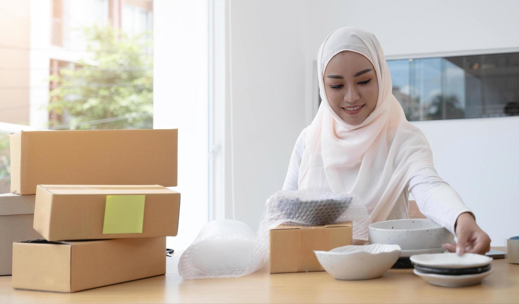 Muslim Business owner woman working online shopping prepare product packaging process at the office, young entrepreneur concept. photo
