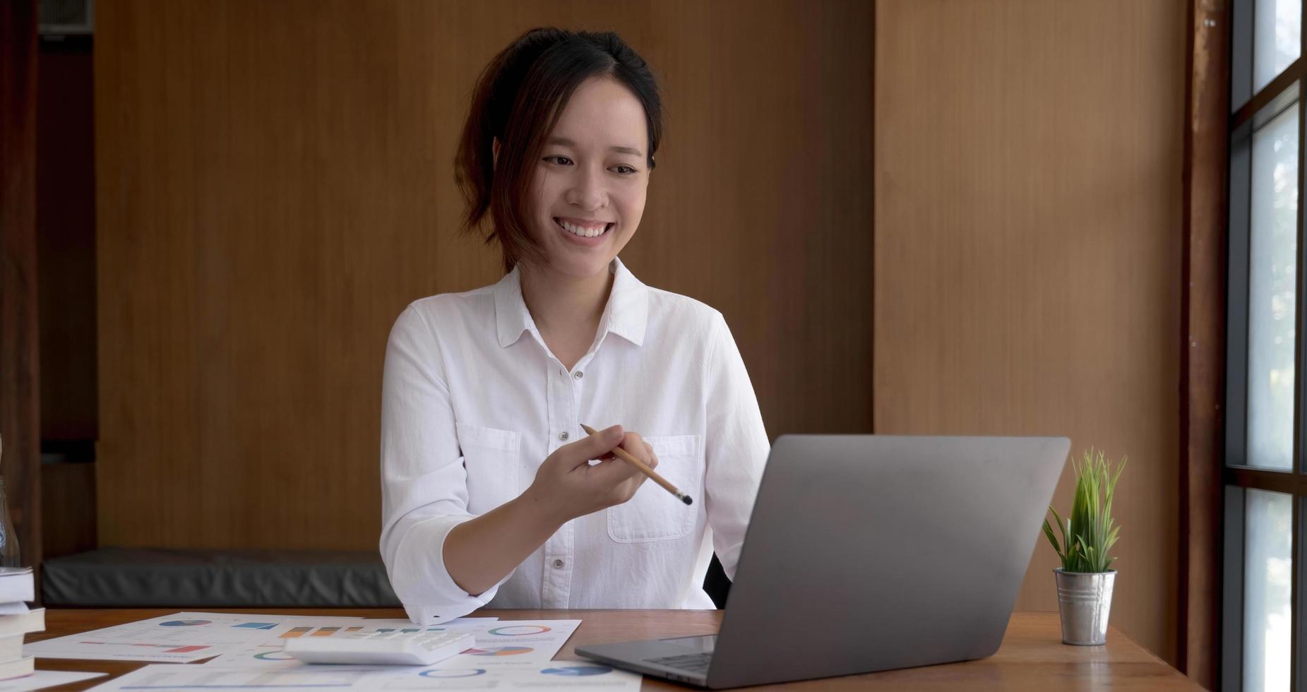 Pretty asian woman fiddling with pen and thinking over a subject while sitting in some coffee shop with her laptop, location public. photo