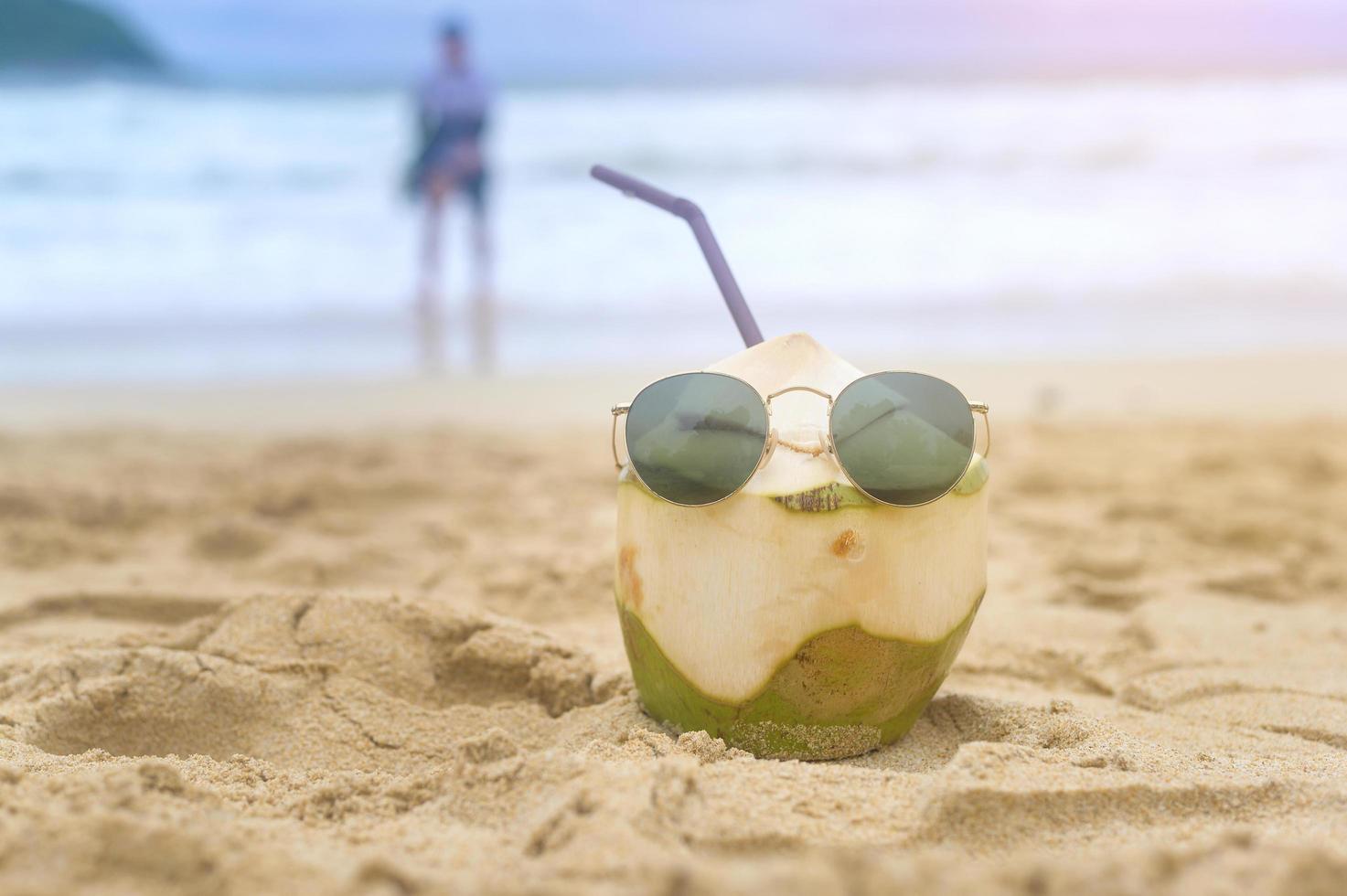 Fresh coconut with drinking straw on the beach, travel and holidays concept. photo